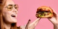 Close up portrait of a hungry young woman eating burger over pink background