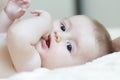 Close up portrait of infant sucking thumb and lying on white bed Royalty Free Stock Photo