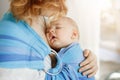 Close up portrait of innocent newborn boy having sweet dreams on mother chest in baby sling. Mom looking at her child