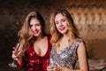Close-up portrait of interested good-looking ladies standing on dark background with wine. Adorable female models in Royalty Free Stock Photo