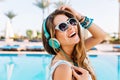 Close-up portrait of joyful laughing young lady in trendy bracelets posing with hand up near the open-air blue swimming Royalty Free Stock Photo