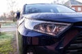 A close up portrait of the left headlight of a dark blue hybrid toyota rav4 car parked on a driveway. The vehicle can drive