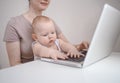 Close up portrait little baby boy funny facial expression sitting on mother`s lap studying laptop. Young mom work from home with