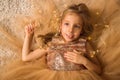 Close up. Portrait of a little beautiful girl, framed by a lush golden dress and luminous lights. Christmas concept Royalty Free Stock Photo