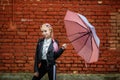 Close up portrait of little beautiful stylish kid girl with an umbrella in the rain near red brick wall as background Royalty Free Stock Photo