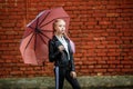 Close up portrait of little beautiful stylish kid girl with an umbrella in the rain near red brick wall as background Royalty Free Stock Photo