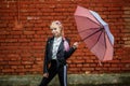 Close up portrait of little beautiful stylish kid girl with an umbrella in the rain near red brick wall as background Royalty Free Stock Photo