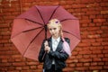 Close up portrait of little beautiful stylish kid girl with an umbrella in the rain near red brick wall as background