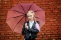 Close up portrait of little beautiful stylish kid girl with an umbrella in the rain near red brick wall as background Royalty Free Stock Photo