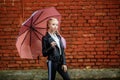 Close up portrait of little beautiful stylish kid girl with an umbrella in the rain near red brick wall as background Royalty Free Stock Photo