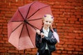 Close up portrait of little beautiful stylish kid girl with an umbrella in the rain near red brick wall as background Royalty Free Stock Photo