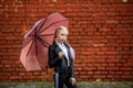 Close up portrait of little beautiful stylish kid girl with an umbrella in the rain near red brick wall as background Royalty Free Stock Photo