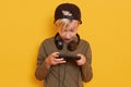 Close up portrait of little blond boy posing with mobile phone in hand isolated over yellow,, studio background, having astonished Royalty Free Stock Photo