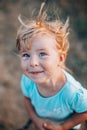 Close up portrait of little blonde girl with blue eyes outside with tousled hair and smiling dirty face. Childhood in the country Royalty Free Stock Photo