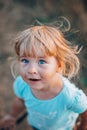 Close up portrait of little blonde girl with blue eyes outside with tousled hair and surprised dirty face. Childhood in the Royalty Free Stock Photo