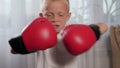 Close-up of a little boy in boxing gloves practicing punches at home.