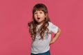 Close-up portrait of a little brunette girl dressed in a white t-shirt posing against a pink studio background. Sincere Royalty Free Stock Photo