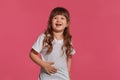 Close-up portrait of a little brunette girl dressed in a white t-shirt posing against a pink studio background. Sincere Royalty Free Stock Photo