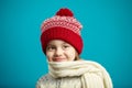 Close up portrait of little charming girl in red winter hat and wrapped scarf on blue background. Royalty Free Stock Photo