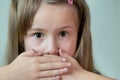 Close-up portrait of little child girl with long hair covering her mouth with hands Royalty Free Stock Photo