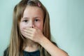 Close-up portrait of little child girl with long hair covering her mouth with hands Royalty Free Stock Photo