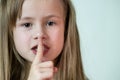 Close-up portrait of little child girl with long hairholding point finger to her lips making hush gesture