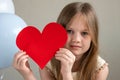 Close up portrait of little cute girl holding big red heart near air balloons. Valentines Day, love, mothers fathers Day