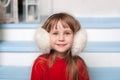 Close up portrait of a little cute girl in a red sweater sitting on porch of house in a winter. smiling child sits on a wooden sta Royalty Free Stock Photo