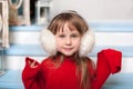 Close up portrait of a little cute girl in a red sweater sitting on porch of house in a winter. smiling child sits on a wooden sta Royalty Free Stock Photo
