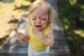 Close up portrait of little funny cute blonde girl child toddler in yellow bodysuit crying outside at summer. Childish Royalty Free Stock Photo