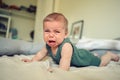 Close up portrait of little funny cute blonde infant boy child toddler with blue eyes in green linen bodysuit crying Royalty Free Stock Photo