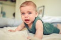 Close up portrait of little funny cute blonde infant boy child toddler with blue eyes in green linen bodysuit crying Royalty Free Stock Photo