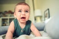 Close up portrait of little funny cute blonde infant boy child toddler with blue eyes in green linen bodysuit crying Royalty Free Stock Photo