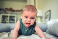 Close up portrait of little funny cute blonde infant boy child toddler with blue eyes in green linen bodysuit crying Royalty Free Stock Photo