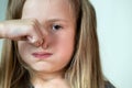 Close-up portrait of little girl with long hair holding her nose with fingers in disgust