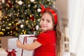 Close-up portrait Little girl in a red dress laughs and enjoys the gift. Little girl opening a magical christmas present at home.