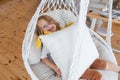 Close-up portrait of little girl riding on swing on macrame chair at home. Child is fooling around