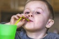 Close up portrait of little kid in the kitchen at home. Pretty child drinks a cold drink from a green plastic cup through a straw. Royalty Free Stock Photo