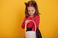 Close up portrait of little pretty girl posing with pink basket in  over yellow background, wearing red sweater and black Royalty Free Stock Photo