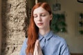 Close-up portrait of long-haired redhead woman posing for a portrait with closed eyes and folded hands