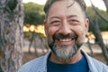 Close up portrait looking on camera of adult mature man with beard and big smile at the park. Aged male person in cheerful Royalty Free Stock Photo