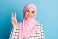 Close-up portrait of lovely cute cheerful muslimah girl showing v-sign isolated over vivid blue color background Royalty Free Stock Photo