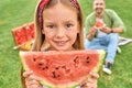 Close up portrait of lovely little girl looking at camera while holding watermelon slice, having a picnic with her daddy Royalty Free Stock Photo