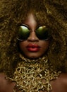 Close-up portrait of magic golden african american female model in massive sunglasses with bright glitter makeup, glossy Royalty Free Stock Photo