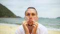 Close-up portrait man apply sun cream protection lotion, looking at camera. Funny man on beach near sea smearing Royalty Free Stock Photo