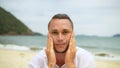 Close-up portrait man apply sun cream protection lotion, looking at camera. Funny man on beach near sea smearing Royalty Free Stock Photo