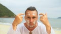 Close-up portrait man apply sun cream protection lotion, looking at camera.Stylish man on beach near sea smearing Royalty Free Stock Photo