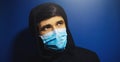 Close-up portrait of man looking up, wearing medical protective flu mask and hooded sweatshirt, on background of dark blue color. Royalty Free Stock Photo