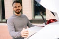 Close-up portrait of man standing near car looking at camera, large white box with red bow at truck.