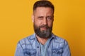 Close up portrait of masculinity handsome bearded man looking directly at camera, standing against yellow background, guy having